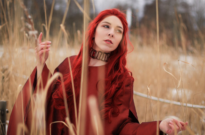 Cosplayer als Melisandre aus Game of Thrones steht in einem Feld aus Schilf.