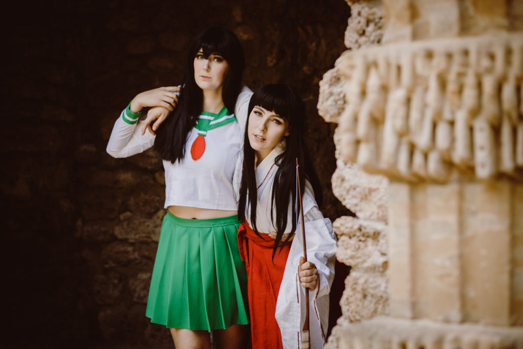 Zwei Cosplayer als Kagome und Kikyo aus InuYasha. Kagome stützt Kikyo, die den Arm um Kagomes Schultern gelegt hat.