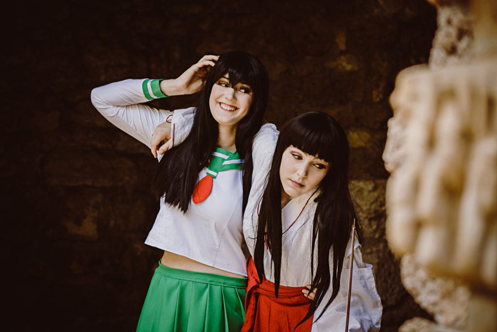 Zwei Cosplayer als Kagome und Kikyo aus InuYasha. Kagome stützt Kikyo, die den Arm um Kagomes Schultern gelegt hat.